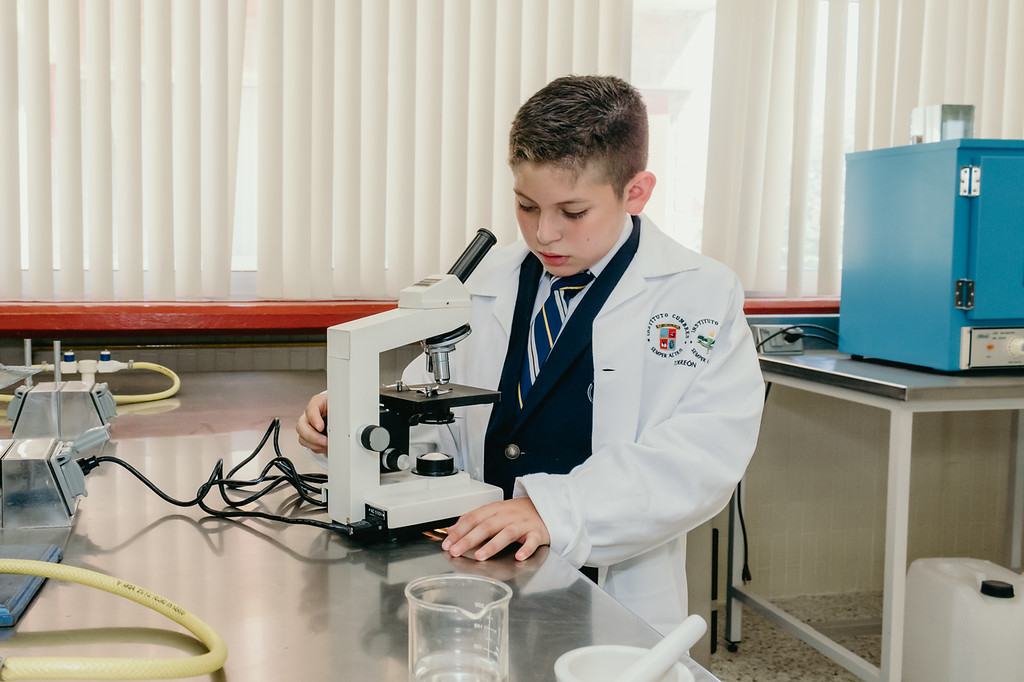 Niño vestido con vata de laboratorio usando un microscopio del instituto cumbres torreon