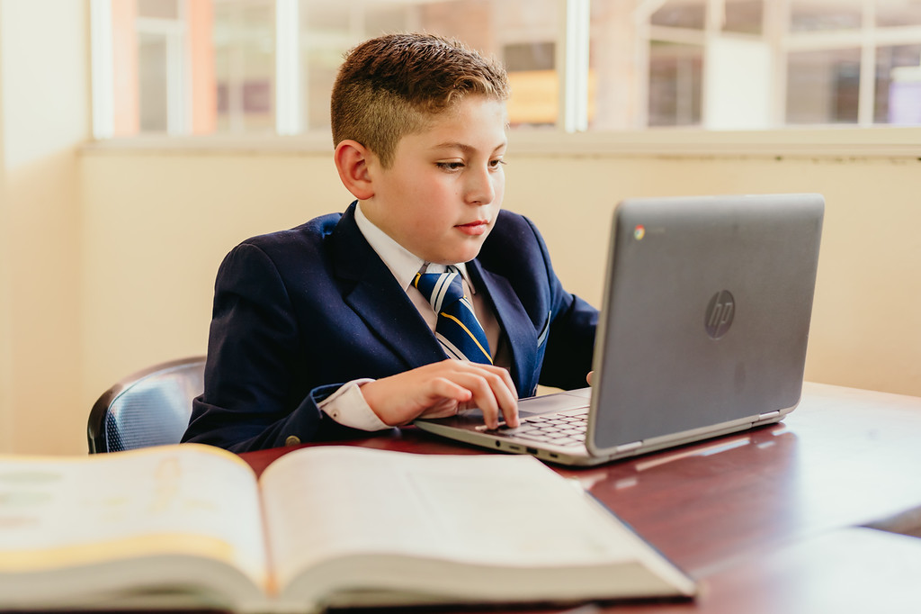 Elementary Niño del instituto en una laptop haciendo sus trabajos dentro de las instalaciones